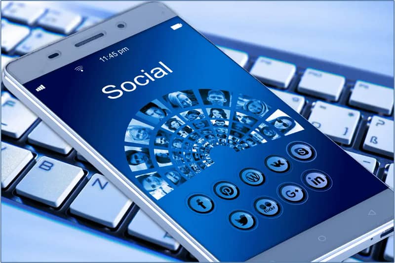 An image of a phone sitting on a keyboard. The phone's screen has social media apps displayed to symbolize social media management.
